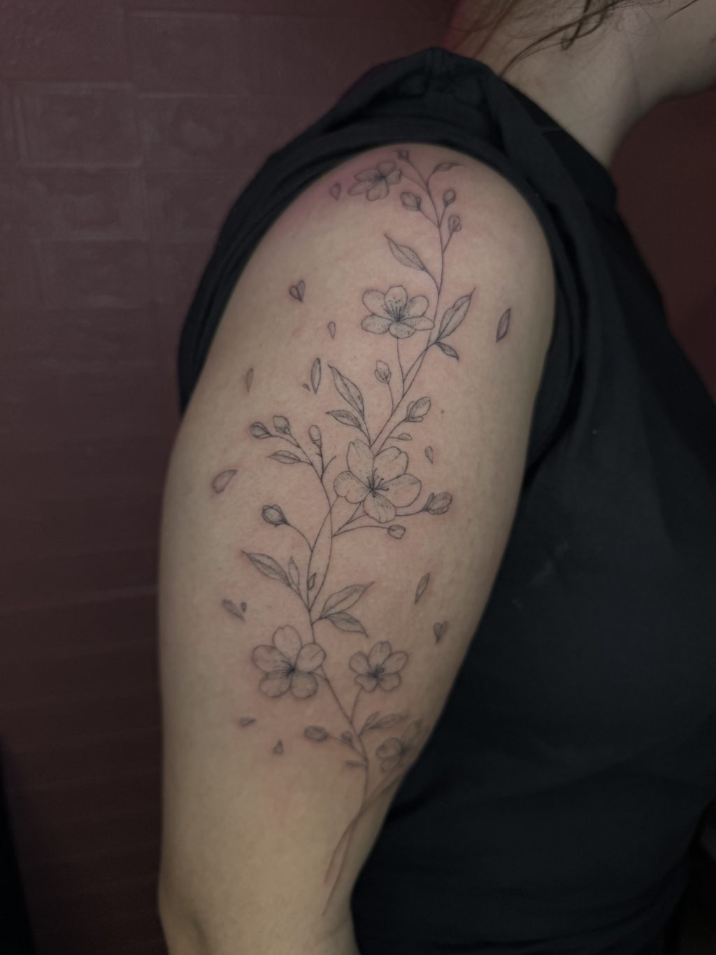 Fine-line black-ink floral branch tattoo on the upper arm.