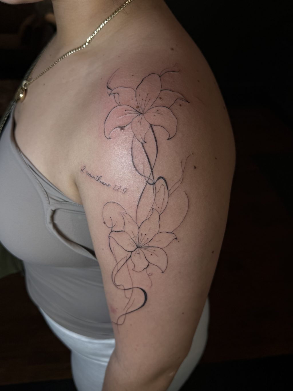Fine-line lilies with small script on the upper arm.