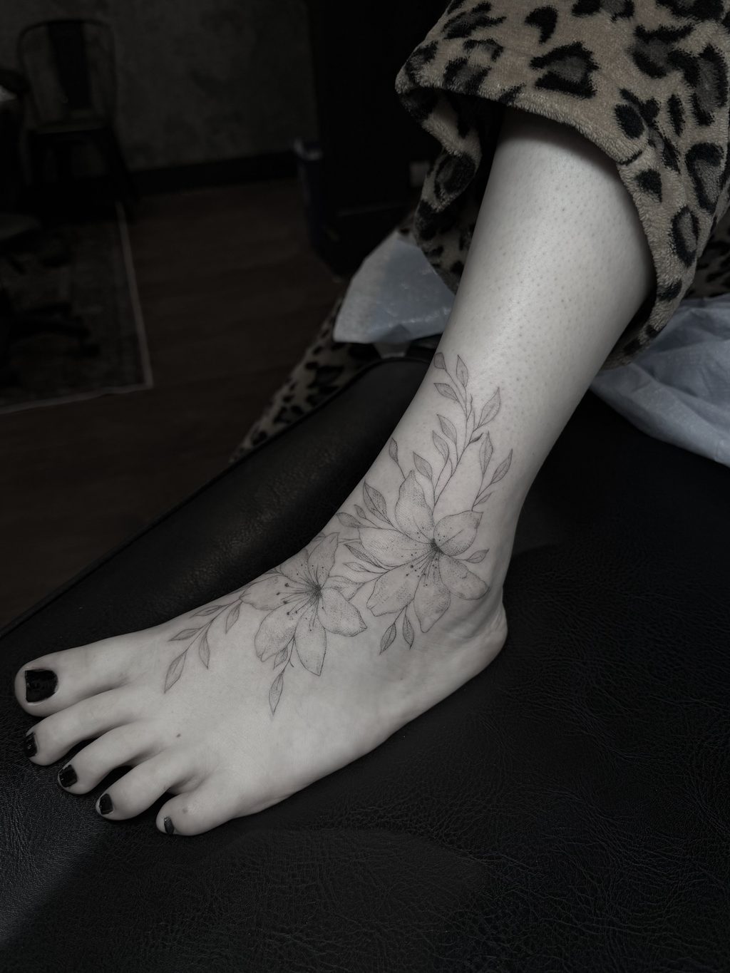 Fine-line floral spray tattoo on the foot.