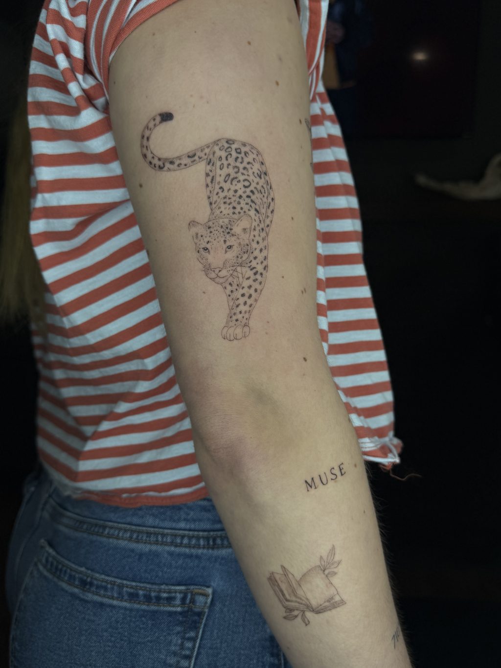 Fine-line leopard linework with script on the forearm.