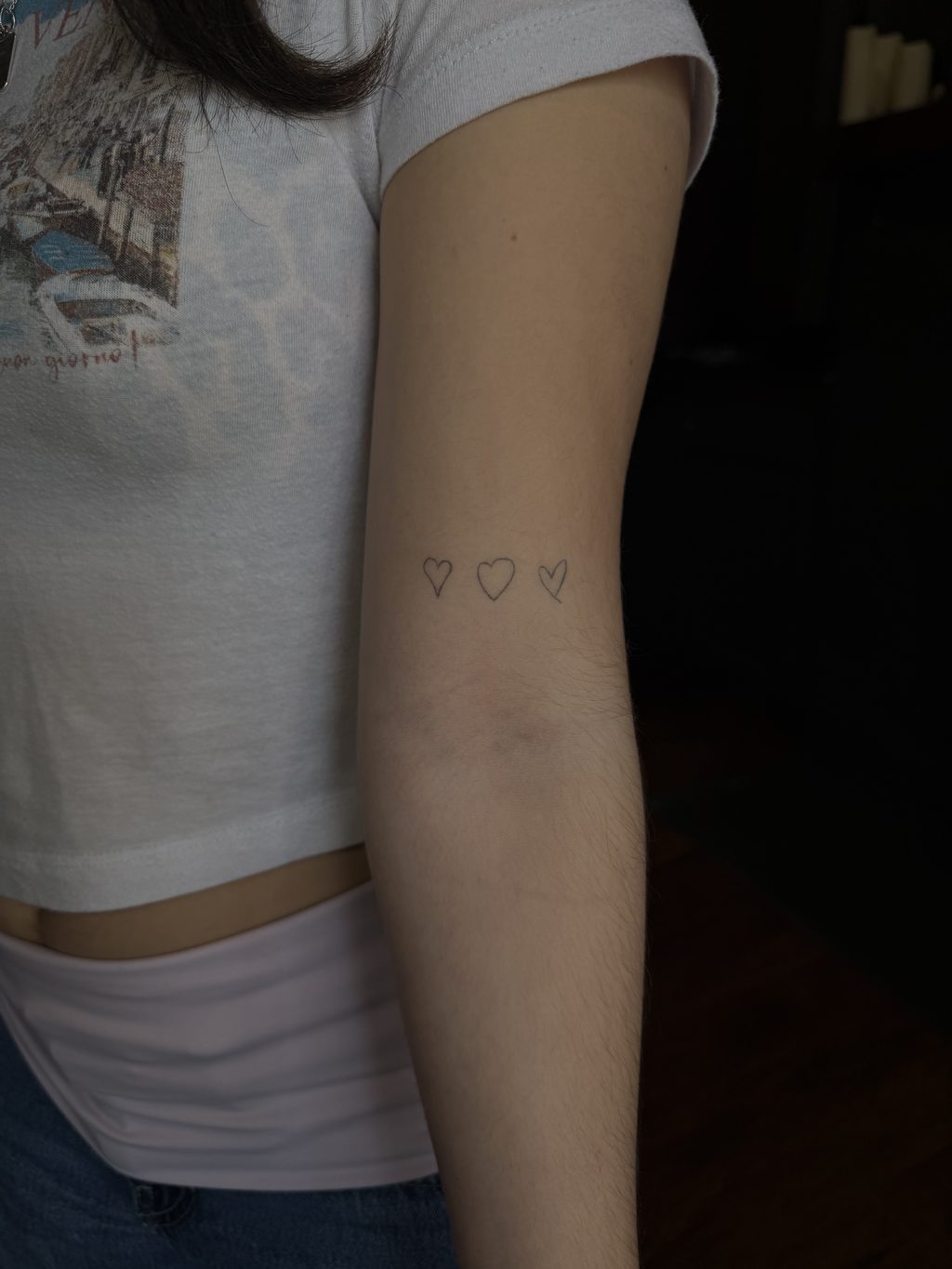 Three small outline heart tattoos on the forearm.