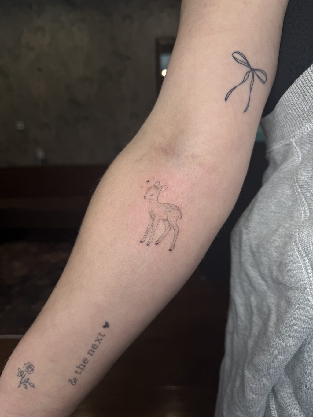 A set of small fine-line tattoos including a bow, fawn, and rose.